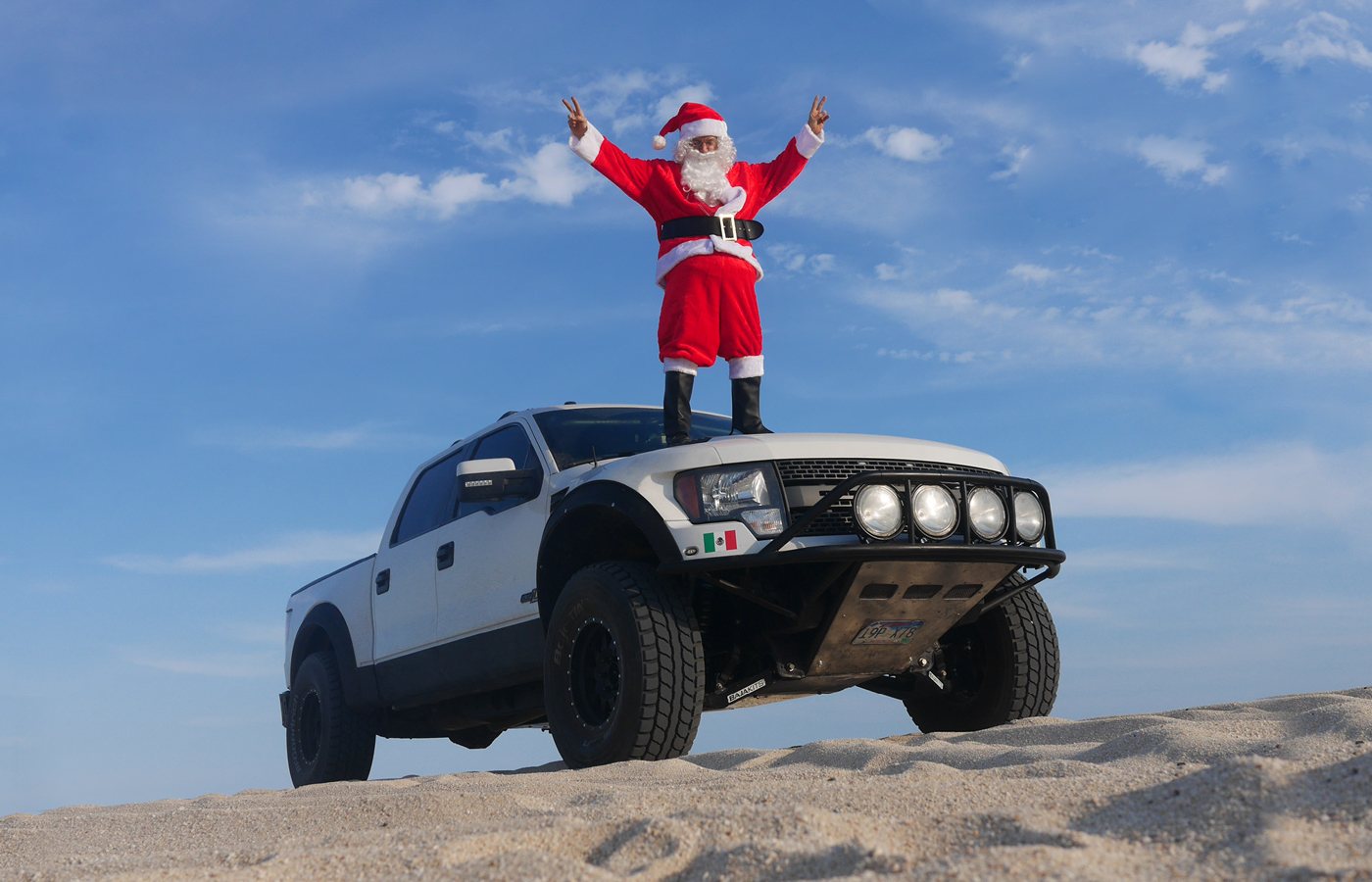 Santa standing on an off-road truck on the sand.