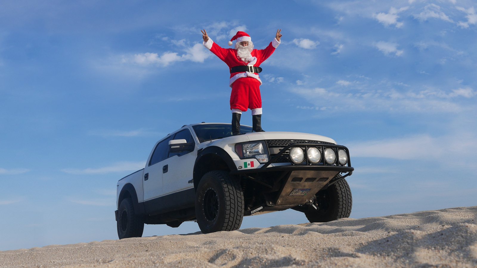 Santa standing on an off-road truck at the beach.